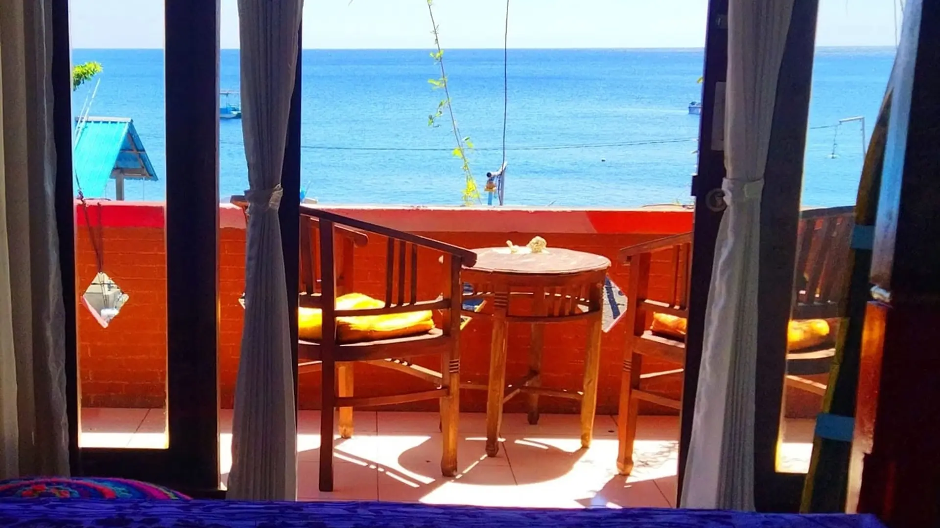 The view from a Pelangi balcony: two chairs, a small table and the sea beyond