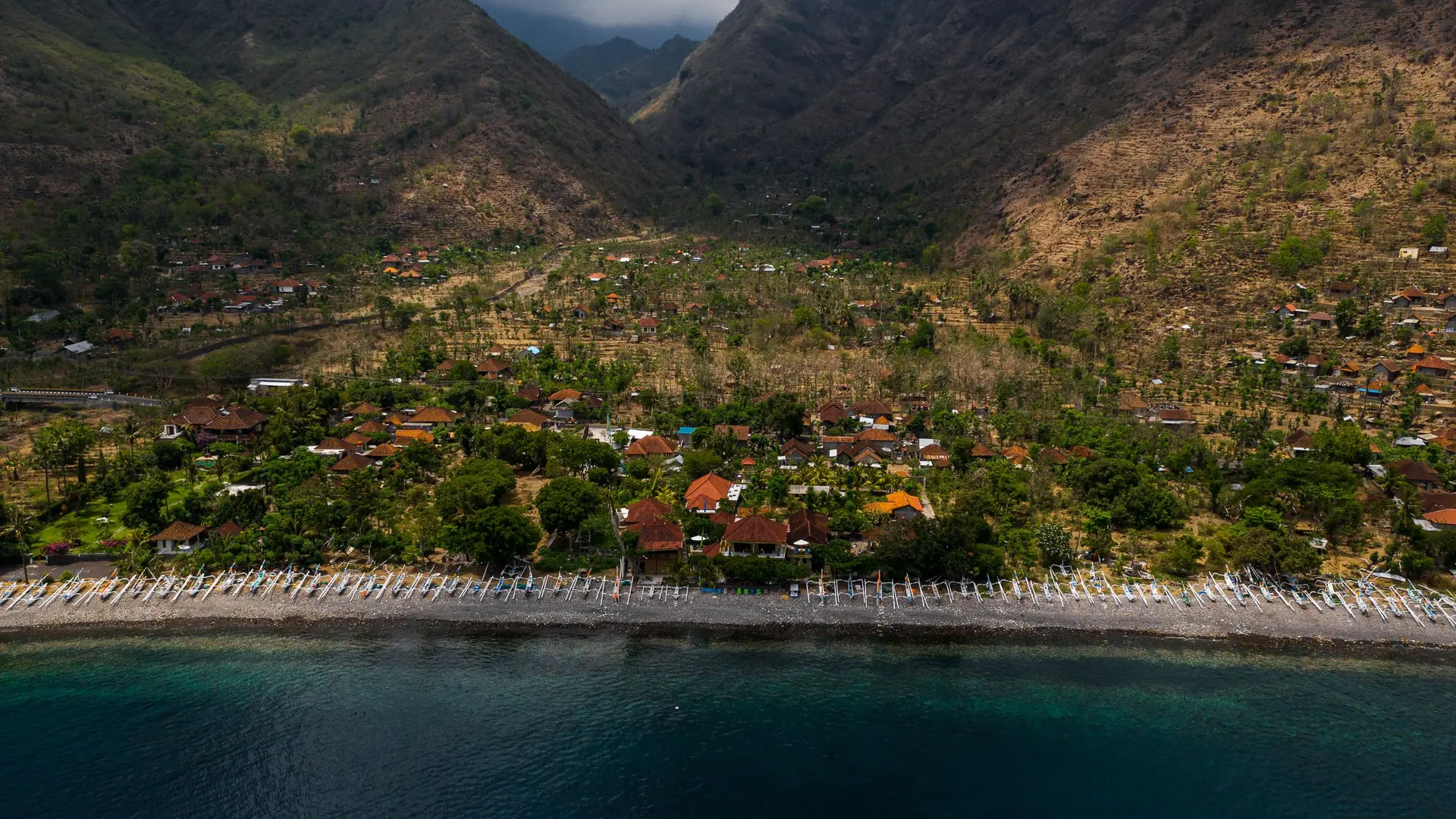 Aerial view of a coastal village between green hills and the sea in East Bali