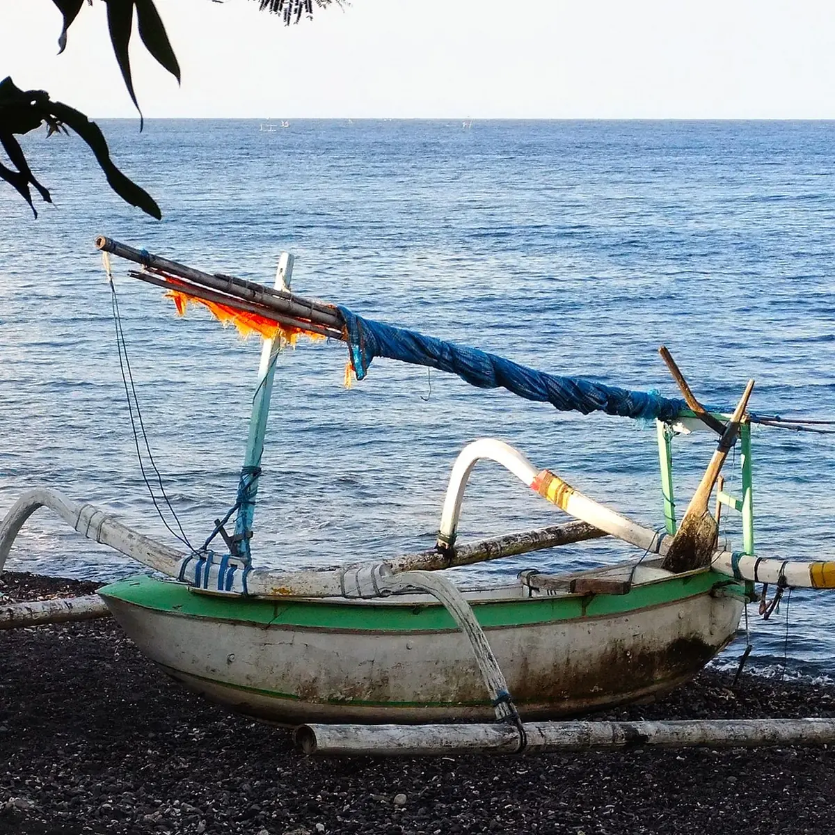 A traditional jukung outrigger boat resting on the dark sand of Amed beach