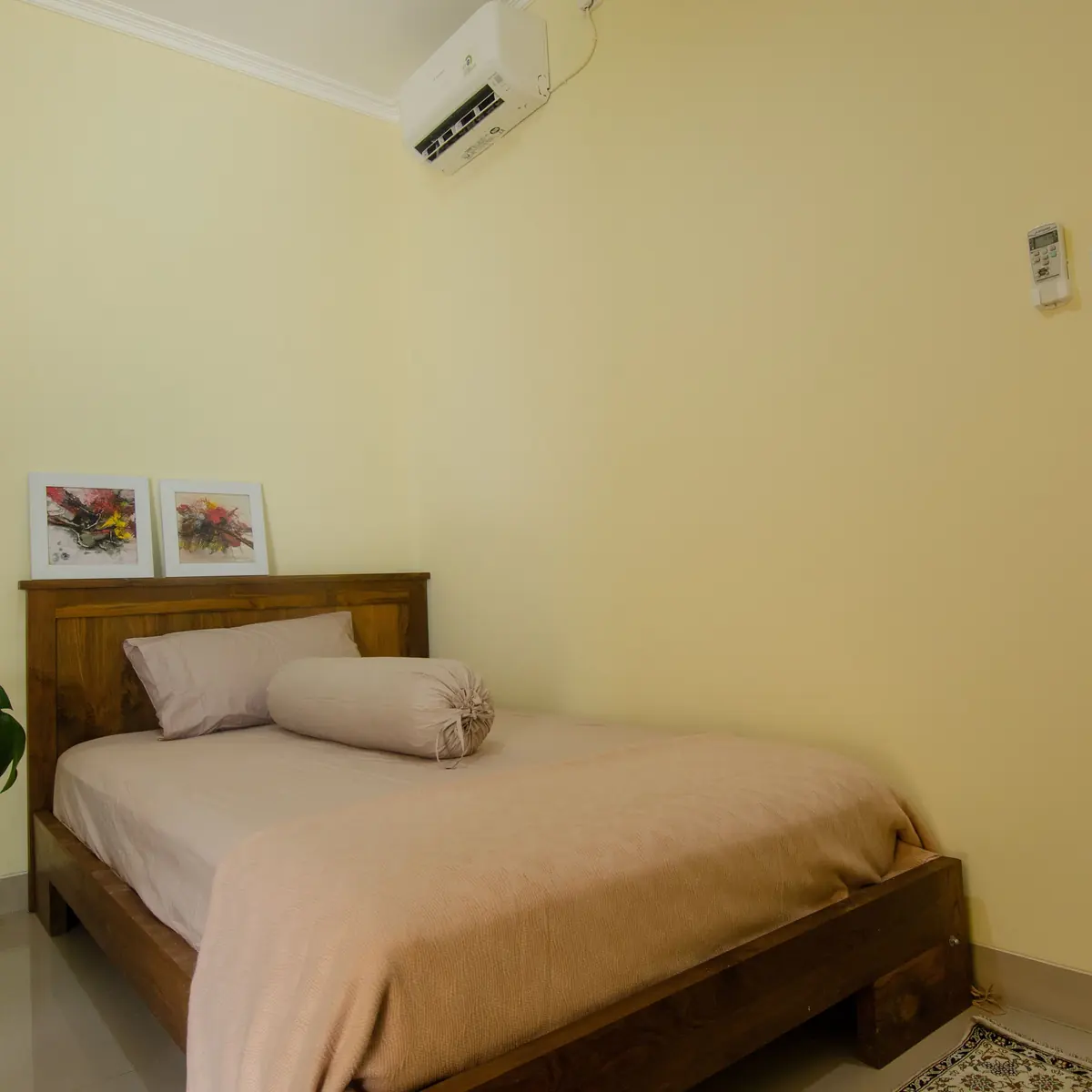 A simple guest room with a double bed and a wall-mounted air conditioner
