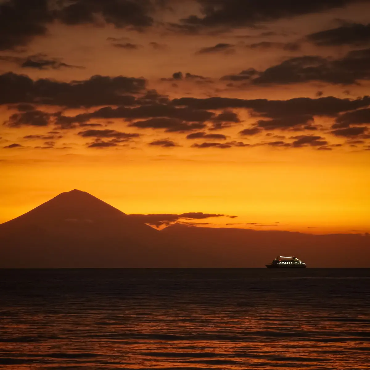 Mount Agung in silhouette against an orange sunset over the sea