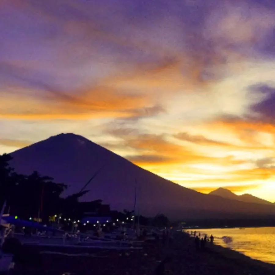 Mount Agung in silhouette at sunset, seen from the beach in Amed with boats along the shore